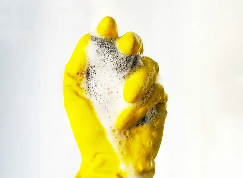 A cleaner's gloved hand holding a soapy sponge