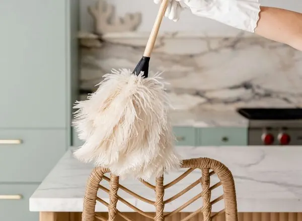 A cleaner dusting high surfaces in a kitchen